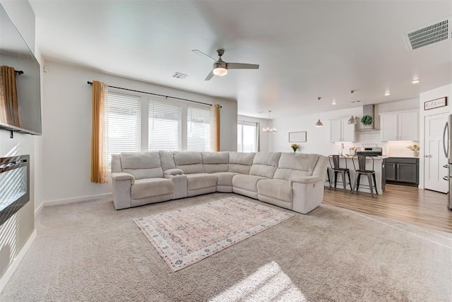 carpeted living room with ceiling fan with notable chandelier