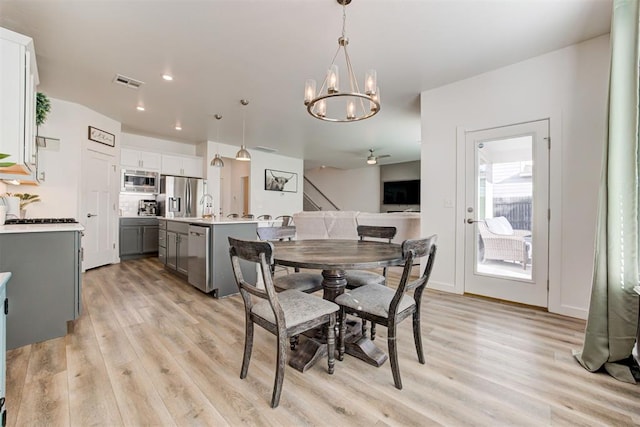 dining room featuring ceiling fan with notable chandelier and light hardwood / wood-style flooring