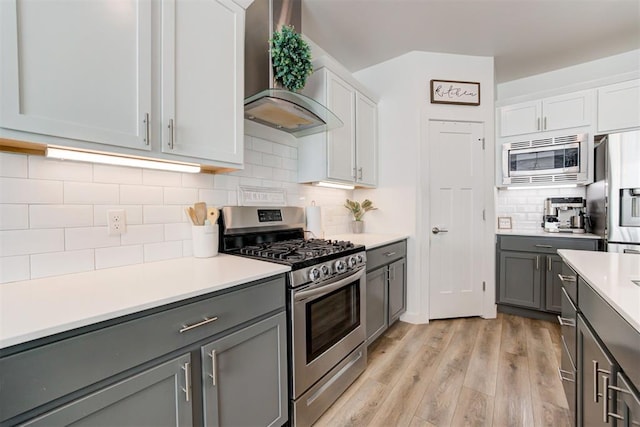 kitchen featuring white cabinetry, light hardwood / wood-style flooring, wall chimney exhaust hood, and appliances with stainless steel finishes