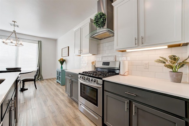 kitchen with wall chimney range hood, stainless steel range with gas cooktop, hanging light fixtures, and white cabinets