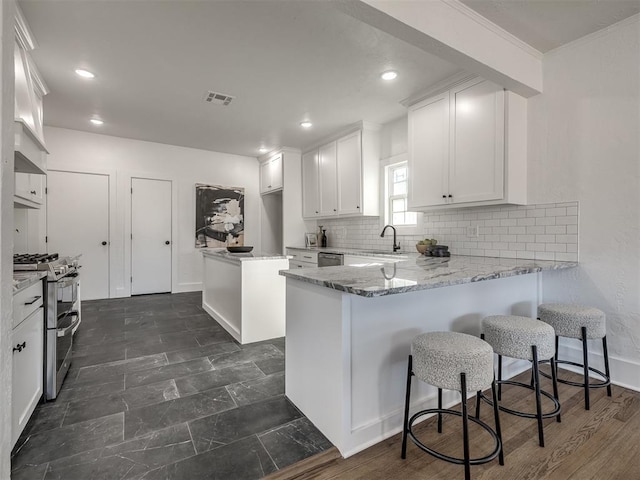 kitchen featuring light stone counters, stainless steel appliances, a peninsula, white cabinets, and decorative backsplash