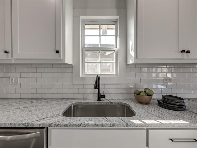 kitchen featuring white cabinets, dishwasher, light stone counters, a sink, and backsplash