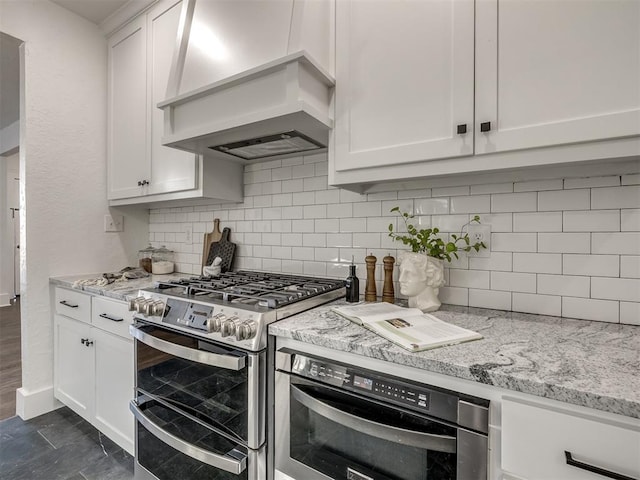 kitchen with white cabinets, light stone counters, premium range hood, oven, and double oven range