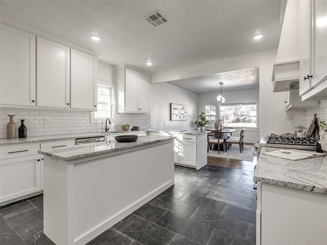 kitchen featuring hanging light fixtures, light stone countertops, white cabinetry, and a center island