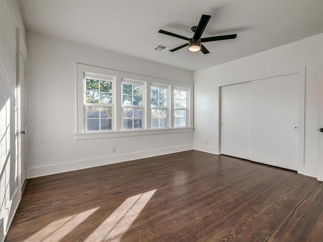 unfurnished bedroom with a closet, dark wood-style flooring, visible vents, and baseboards