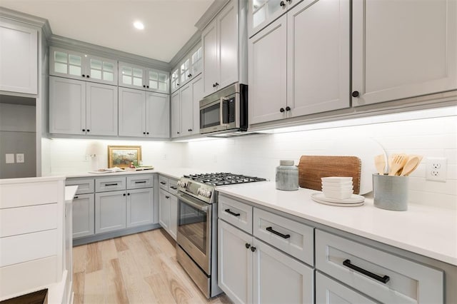 616 Montauk Way, Edmond, OK 73034 - kitchen featuring appliances with stainless steel finishes, light wood-style flooring, glass insert cabinets, and gray cabinets