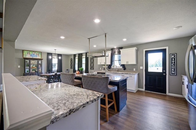 kitchen with white cabinetry, light stone countertops, hanging light fixtures, and a kitchen island