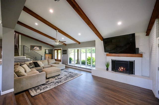 living room featuring dark wood-type flooring, ceiling fan, a brick fireplace, and vaulted ceiling with beams