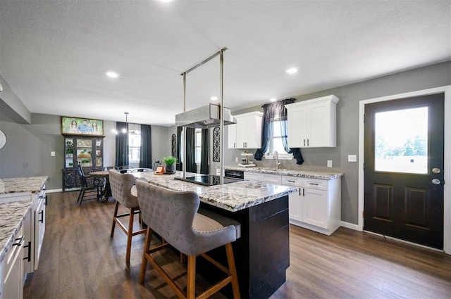 kitchen featuring a kitchen island, decorative light fixtures, white cabinetry, a kitchen bar, and black electric stovetop