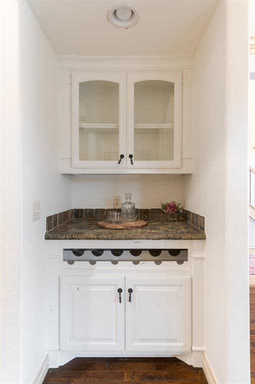 bar with white cabinetry and dark stone countertops