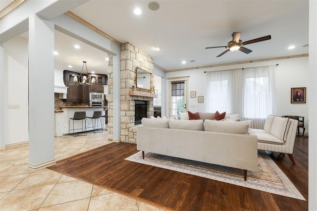 living room featuring light tile patterned flooring, ornamental molding, a fireplace, and ceiling fan with notable chandelier