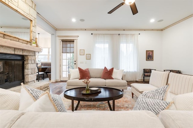 living room with ceiling fan, ornamental molding, a stone fireplace, and hardwood / wood-style floors