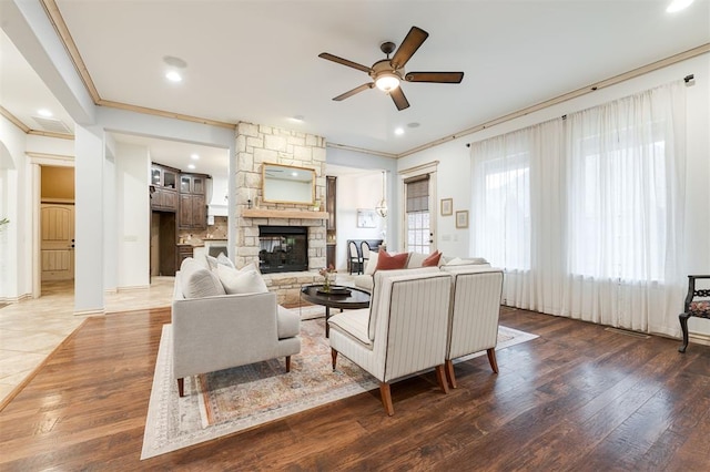 living room with dark hardwood / wood-style floors, ceiling fan, a stone fireplace, and crown molding