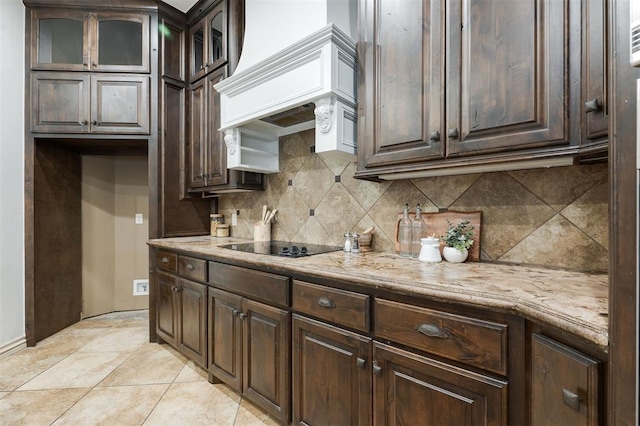 kitchen featuring backsplash, custom exhaust hood, light stone countertops, dark brown cabinets, and black electric cooktop