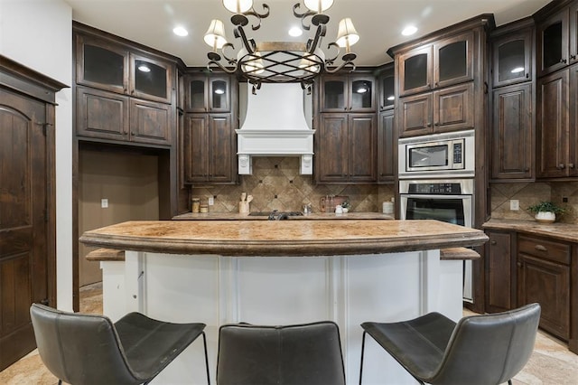 kitchen featuring pendant lighting, dark brown cabinets, a kitchen breakfast bar, stainless steel appliances, and custom exhaust hood