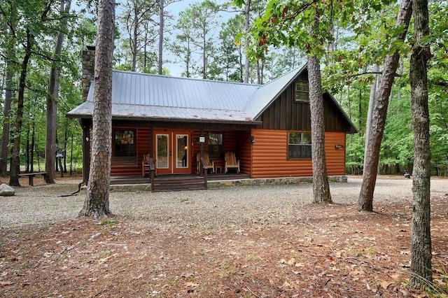 chalet / cabin with metal roof, covered porch, french doors, log veneer siding, and a chimney