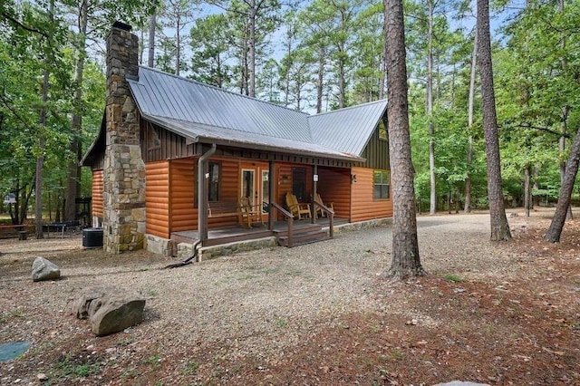 view of front of property featuring covered porch, metal roof, a chimney, and faux log siding