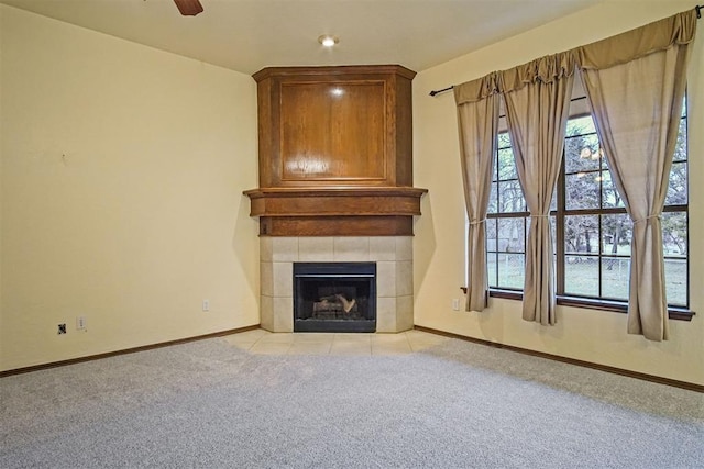 unfurnished living room featuring a tiled fireplace, light colored carpet, and ceiling fan