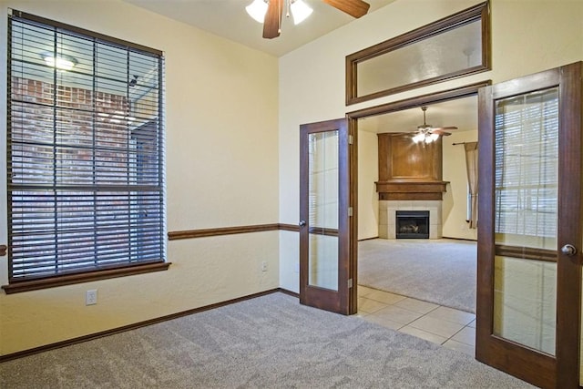 carpeted spare room with a tiled fireplace, a healthy amount of sunlight, french doors, and ceiling fan