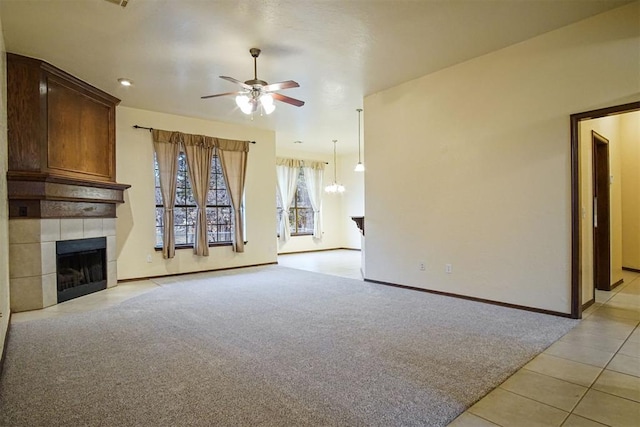 unfurnished living room featuring ceiling fan with notable chandelier, light colored carpet, and a tile fireplace