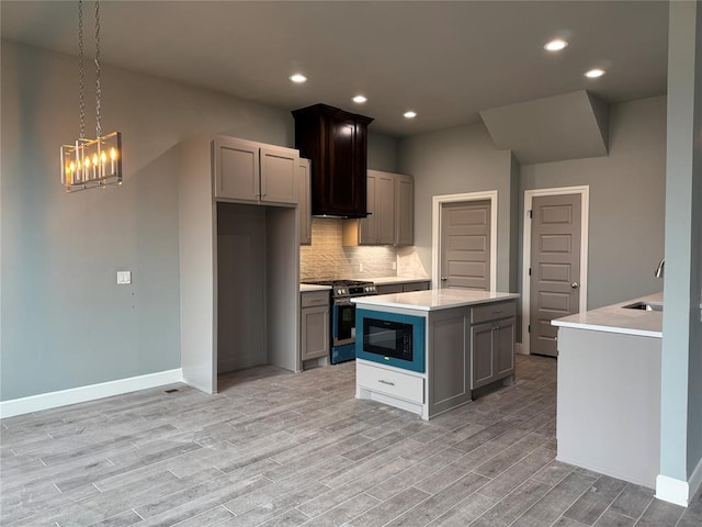 kitchen featuring stainless steel gas range, gray cabinetry, a center island, black microwave, and pendant lighting