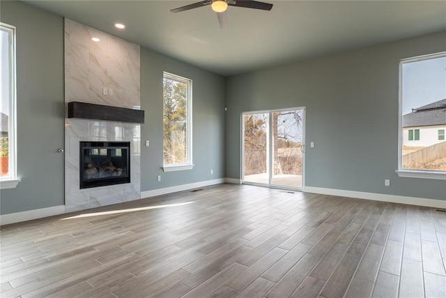 unfurnished living room with baseboards, ceiling fan, a fireplace, and light wood-style floors