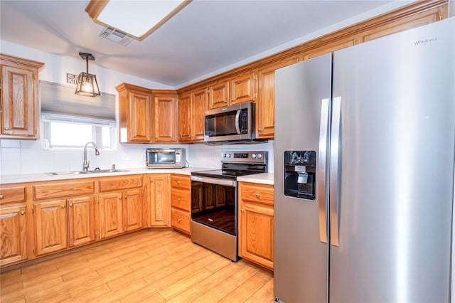 kitchen with pendant lighting, sink, appliances with stainless steel finishes, backsplash, and light hardwood / wood-style floors