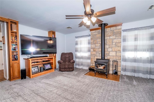 living room with ceiling fan, carpet floors, and a wood stove