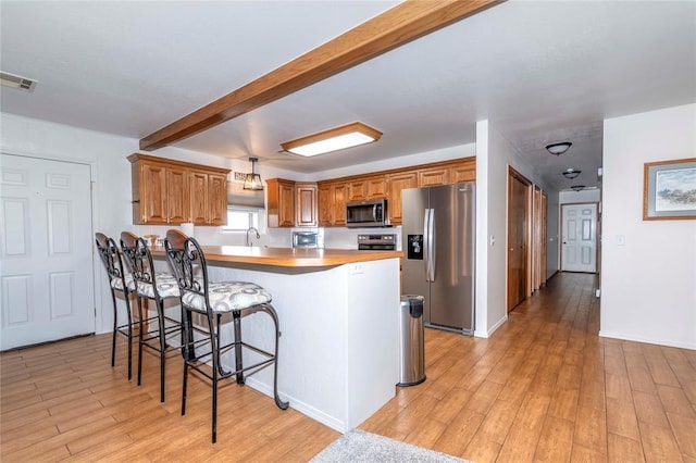 kitchen with a kitchen bar, kitchen peninsula, stainless steel appliances, beam ceiling, and light hardwood / wood-style flooring