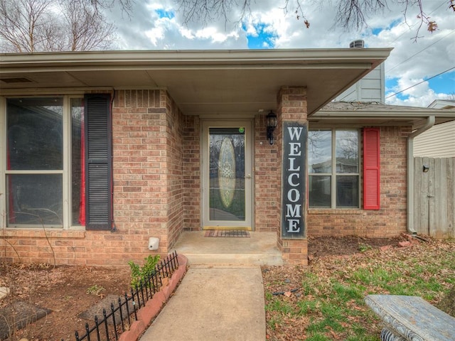 doorway to property featuring brick siding and fence