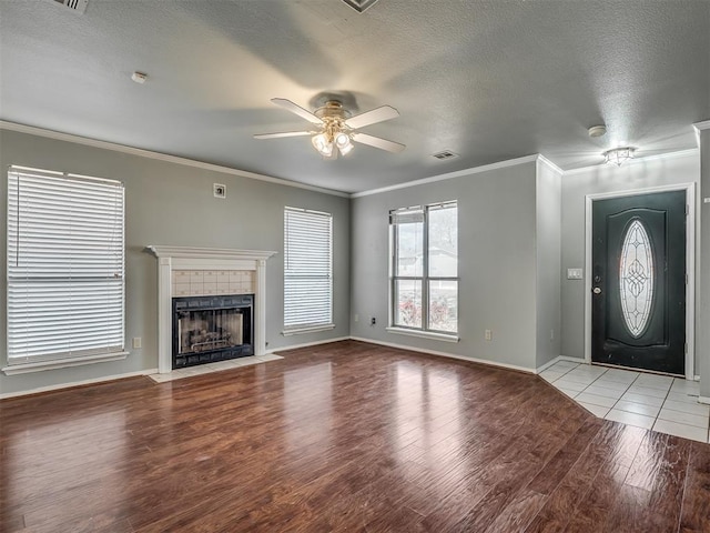 unfurnished living room with crown molding, a textured ceiling, a tiled fireplace, and wood finished floors