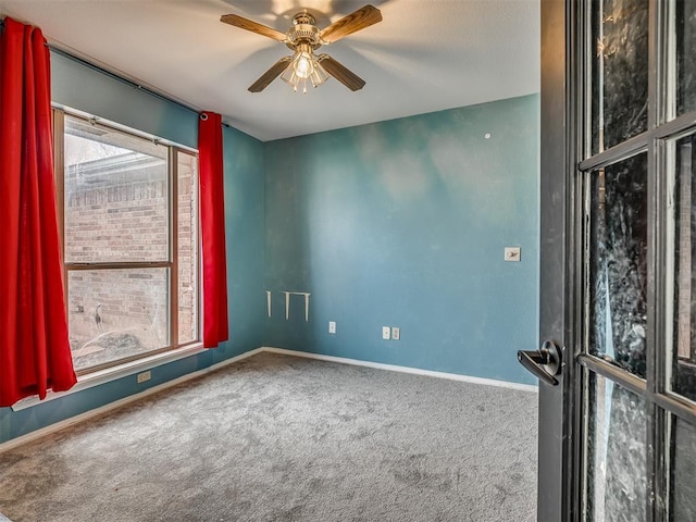 carpeted spare room featuring ceiling fan and baseboards