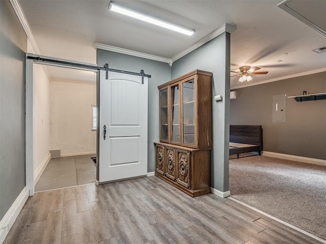 unfurnished room featuring a barn door, baseboards, a ceiling fan, crown molding, and light wood-style floors