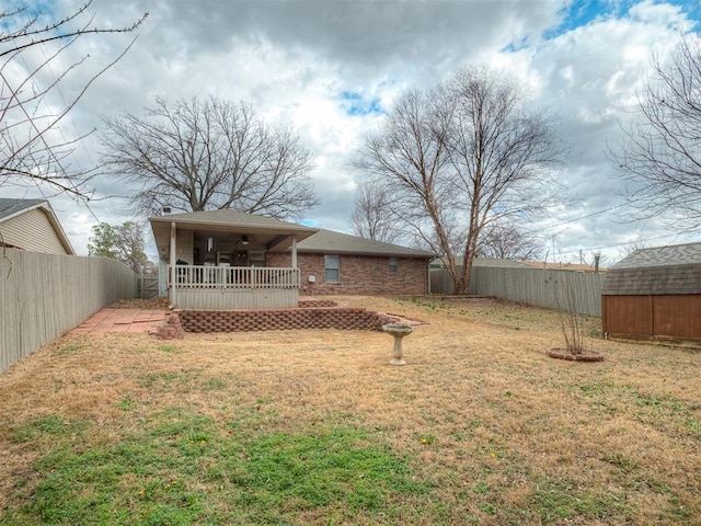 rear view of house with a lawn, a fenced backyard, ceiling fan, an outdoor structure, and brick siding