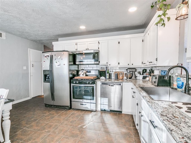 kitchen with sink, a textured ceiling, stainless steel appliances, light stone countertops, and white cabinets