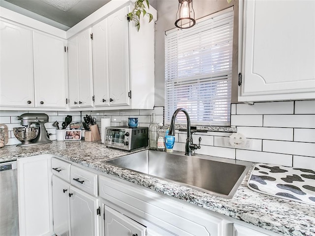 kitchen with tasteful backsplash, stainless steel dishwasher, sink, and white cabinets