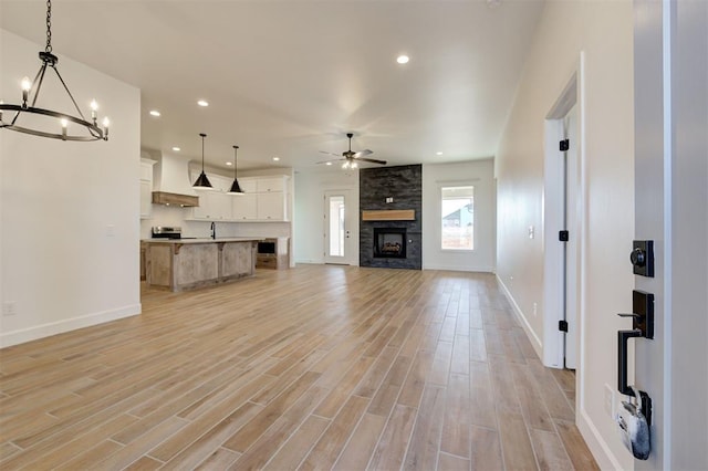 unfurnished living room featuring light wood-type flooring, sink, a large fireplace, and ceiling fan with notable chandelier