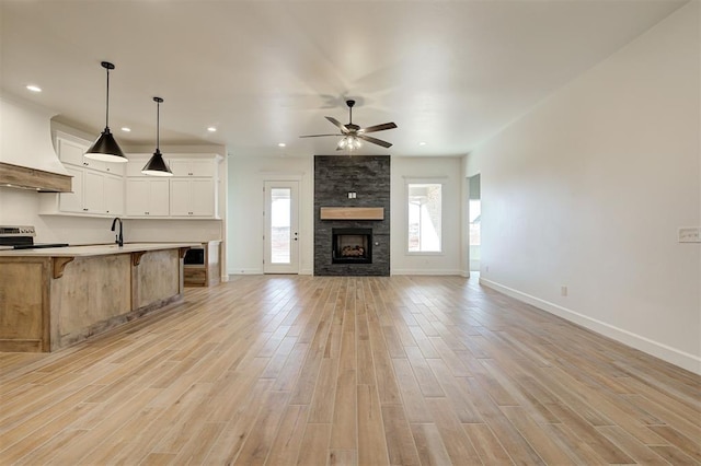 unfurnished living room featuring light hardwood / wood-style flooring, ceiling fan, a stone fireplace, and sink