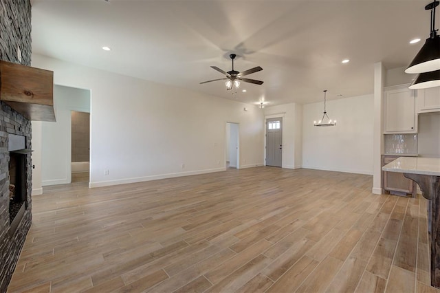 unfurnished living room with ceiling fan with notable chandelier, light wood-type flooring, and a stone fireplace