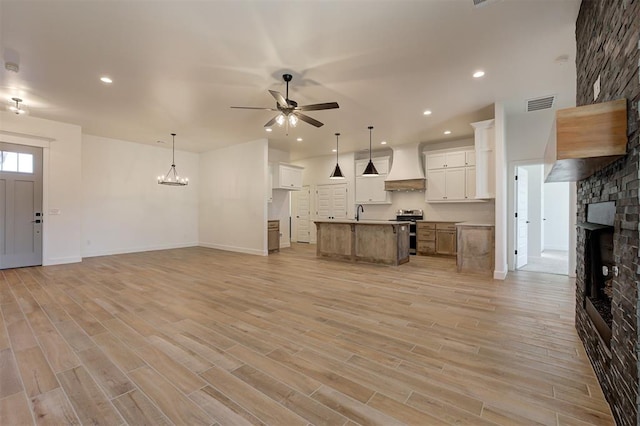 unfurnished living room featuring ceiling fan with notable chandelier, light hardwood / wood-style floors, sink, and a fireplace