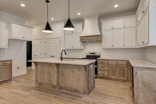 kitchen with a kitchen island with sink, stainless steel range with electric cooktop, hanging light fixtures, custom exhaust hood, and white cabinets