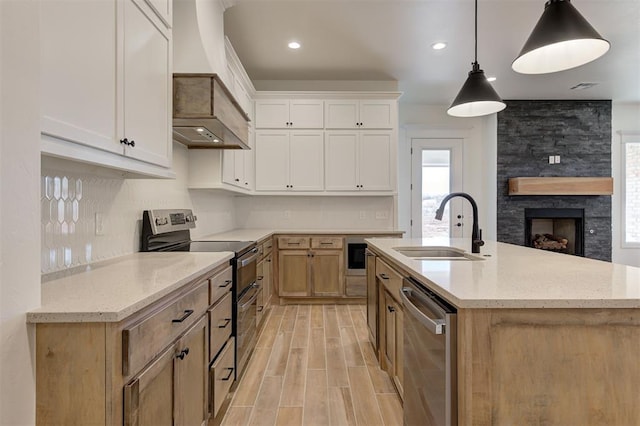 kitchen with appliances with stainless steel finishes, sink, premium range hood, decorative light fixtures, and white cabinets