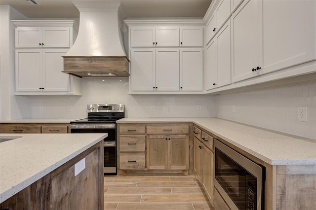 kitchen with range with two ovens, white cabinets, light stone countertops, and custom range hood