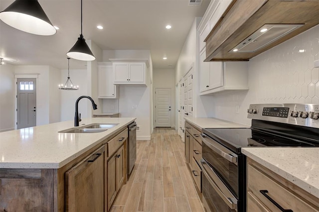 kitchen featuring appliances with stainless steel finishes, hanging light fixtures, white cabinets, sink, and a kitchen island with sink