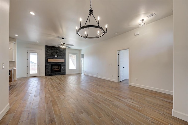 unfurnished living room featuring ceiling fan with notable chandelier, light hardwood / wood-style floors, and a stone fireplace