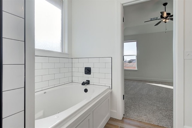 bathroom with a wealth of natural light, ceiling fan, and a tub to relax in