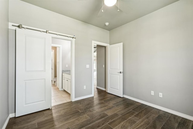 unfurnished bedroom featuring ceiling fan, a barn door, connected bathroom, and dark hardwood / wood-style flooring