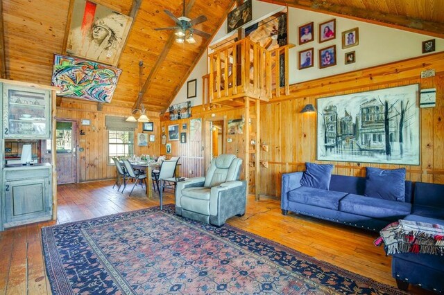 living room with ceiling fan, hardwood / wood-style floors, vaulted ceiling with beams, wooden walls, and wooden ceiling