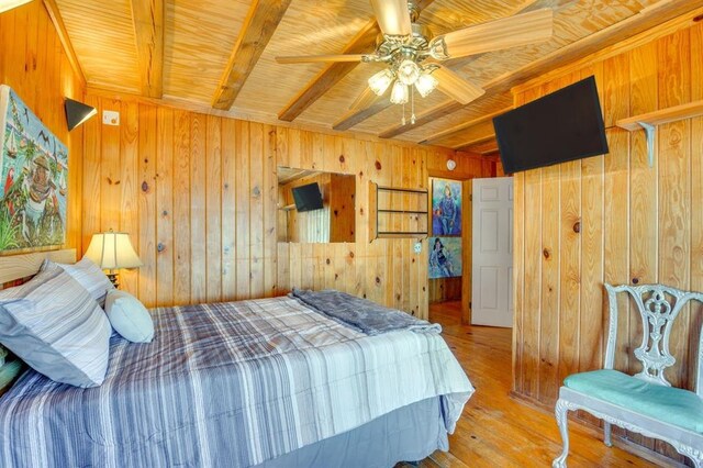 bedroom with wood ceiling, light hardwood / wood-style flooring, wooden walls, ceiling fan, and beam ceiling