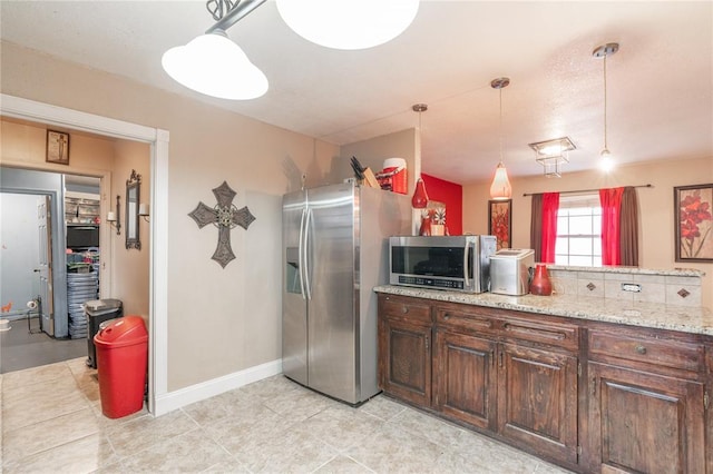 kitchen with light stone counters, dark brown cabinetry, stainless steel appliances, and hanging light fixtures